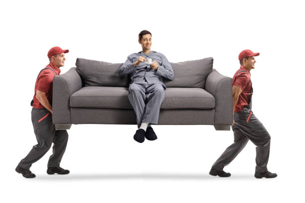 istock Movers carrying a sofa with a man in pajamas sitting and drinking coffee 1294602779