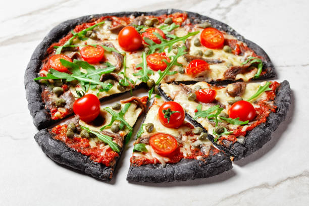 istock black dough pizza with anchovy, melted mozzarella cheese, tomato, rocket salad and capers on a marble table 1294602825