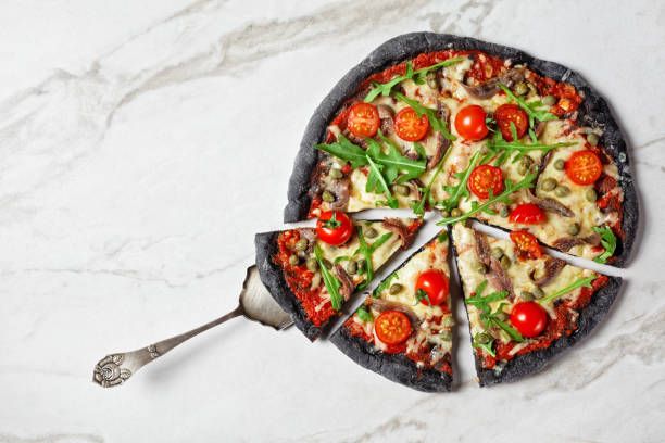 istock black dough pizza with anchovy, melted mozzarella cheese, tomato, rocket salad and capers on a marble table 1294602840