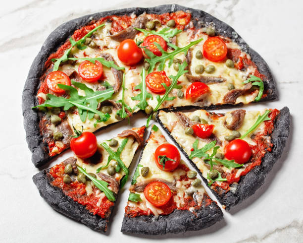 istock black dough pizza with anchovy, melted mozzarella cheese, tomato, rocket salad and capers on a marble table 1294602902