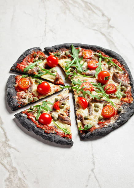 istock black dough pizza with anchovy, melted mozzarella cheese, tomato, rocket salad and capers on a marble table 1294602922