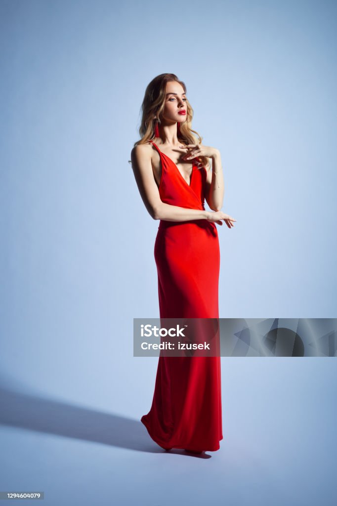 Elegant woman in red dress Glamour portrait of beautiful long blond hair woman wearing red long dress. Studio shot against grey background. One Woman Only Stock Photo