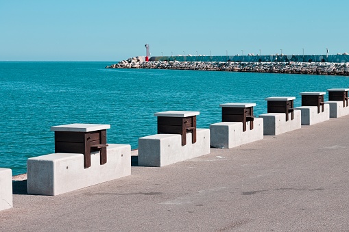 A series of wooden tables with stone benches placed on the edge of the pier of the port of Pesaro (Pesaro, Italy, Europe)