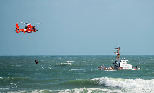 Daytona Beach, FL USA - October 13, 2011: US Coast Guard ship and helicopter, air show performance, blue sky, bright day, moderate sea swells, full shot of rescue scene, swells partially block lower part of Coast guard vessel