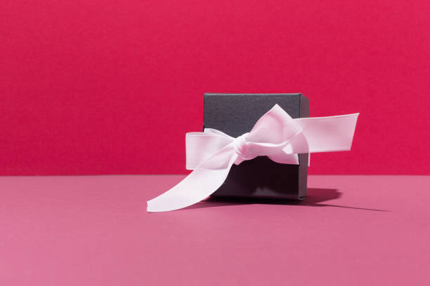 istock Festive Black gift box with white bow on pink background. Holiday time concept. 1294615379