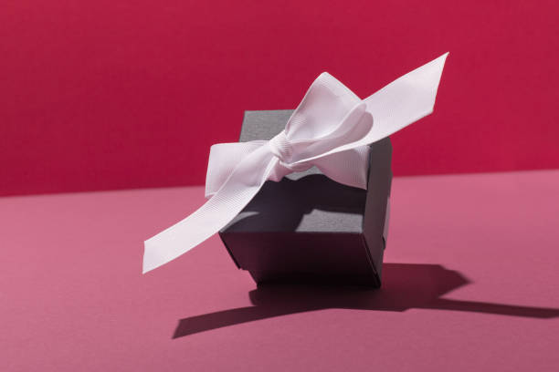 Festive Black gift box with white bow on pink background. Holiday time concept.