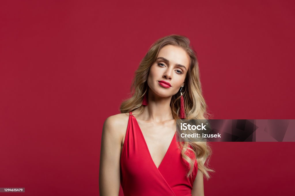 Beautiful woman in red long dress Fashion portrait of beautiful long blond hair woman wearing red dress, smiling at camera. Studio shot against red background. 20-29 Years Stock Photo
