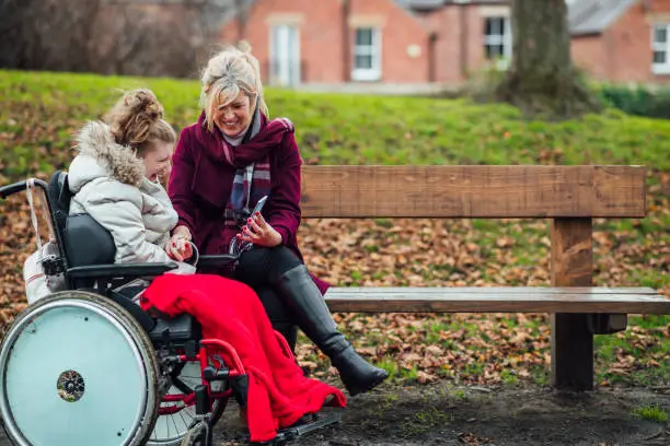 Photo of Mother and Daughter Using Smart Phone on a Park Bench