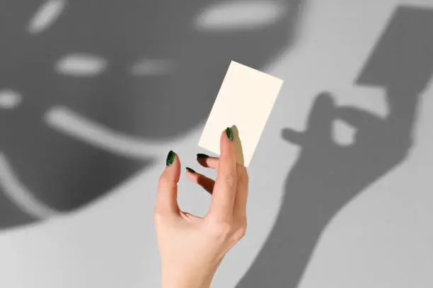 Female hand holding blank businesscard. Creative photo with shadow close up