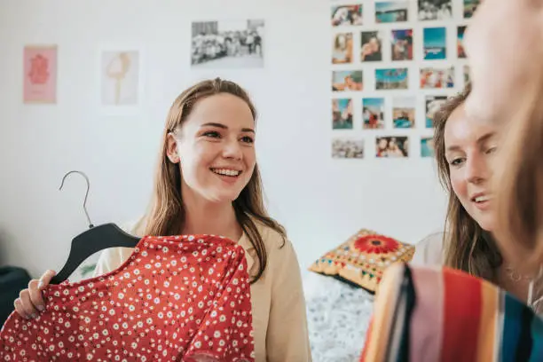 young woman presenting a dress on coat hanger to her female room mates indoors