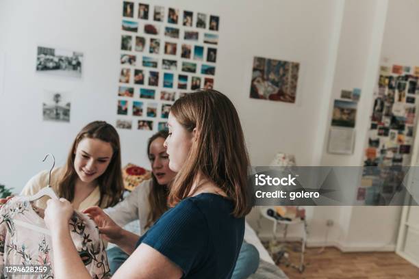 Three Young Woman Showing Clothes From Hatstand To Eachother Stock Photo - Download Image Now