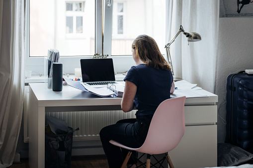 rear view on young woman reading in folder at desk at home