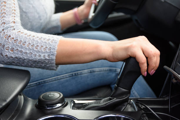 istock Female driver is driving the car. She is shifting gears in automatic gearbox before start moving. Young woman in jeans and sweater is sitting in the car behind the wheel. 1294631300