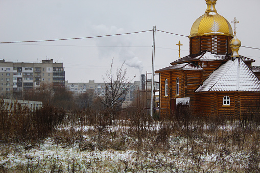 church in the city, in the background a chimney and Soviet buildings are smoking, boring view, low temperature snow