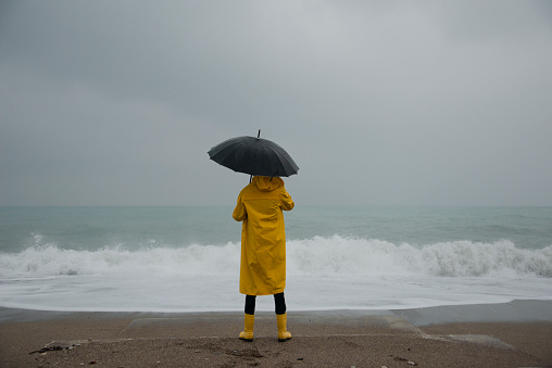 man standing on the beach in stormy weather. The man wearing a yellow raincoat watches the big waves.