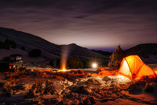 Winter Camping in the Great Outdoors - Dusk and night images with tent glowing outdoors. Campfire in snow staying warm outdoor adventure and recreation.