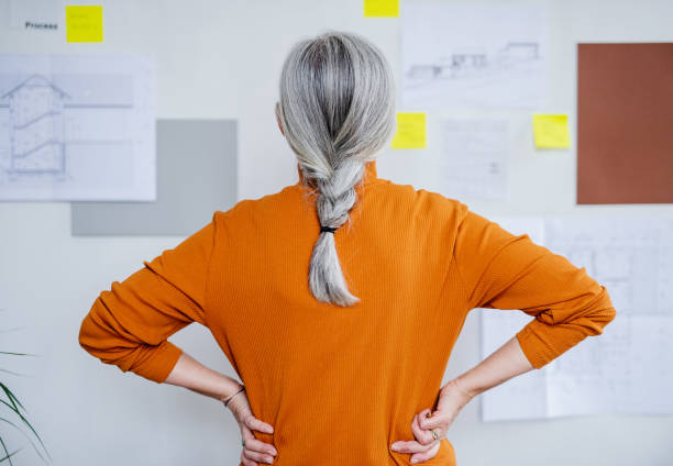 Rear view of senior woman architect standing indoors at home, standing and working. A rear view of senior woman architect standing indoors at home, standing and working. grey hair stock pictures, royalty-free photos & images