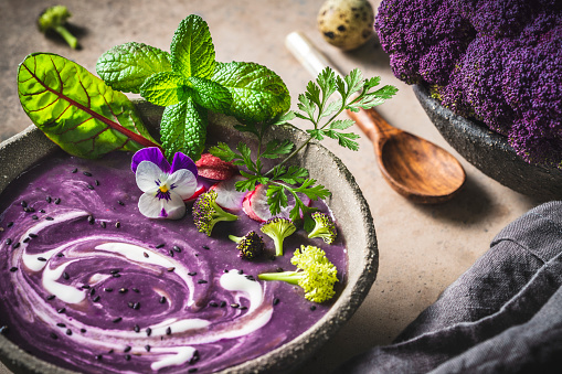 Purple cauliflower soup woth purple potatoes in a bowl with herbs and edible flower