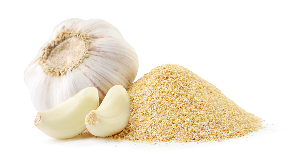 A pile of ground garlic and a head of garlic with cloves close-up on a white background. Isolated