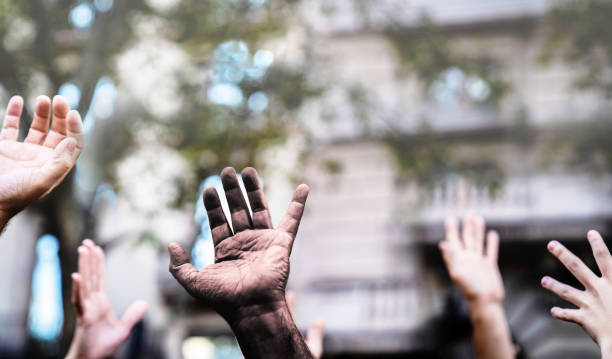 mani multiculturali alzate nell'aria che chiedono libertà in una manifestazione per strada. palmo aperto di una mano nera e mani bianche. fermate il razzismo. fermate la repressione. - anti racism foto e immagini stock