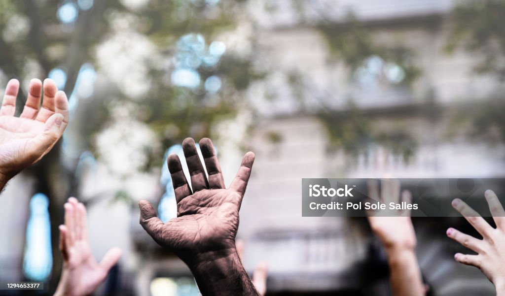 Multicultural hands raised in the air asking for freedom in a demonstration on street.Open palm of a black hand and white hands. Stop racism. Stop repression. Human Rights Stock Photo