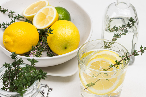 Lemon drink in glass. Thyme sprigs in glass. Lemons on table and in ceramic bowl. Close up. White background. Top view.