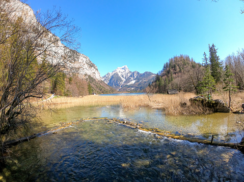 Idyllic view on Leopoldsteiner lake in Austria. The lake is surrounded by high Alps. The shallow water is crystal clear, spring water has a calm surface. Early spring. Serenity. Some snow fields. Calm