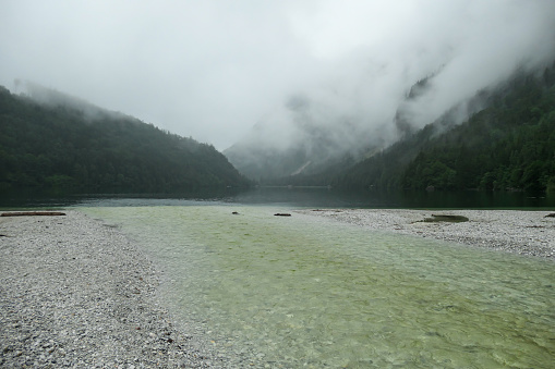Idyllic view on Leopoldsteiner lake in Austria. The lake is surrounded by high Alps, covered in thick fog. Rainy weather. The shallow water is crystal clear, spring water has a calm surface. Serenity