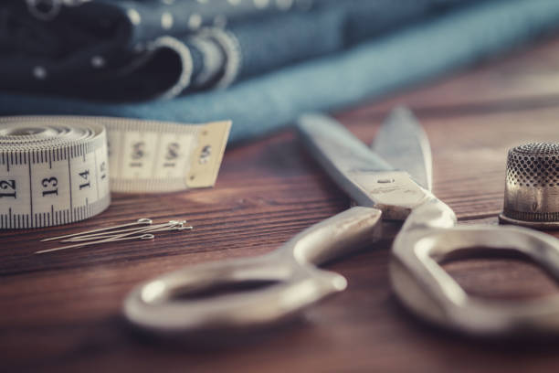 istock Sewing items - tailoring scissors, measuring tape, including pins, thimble. Blue jeans fabrics for sewing on background. 1294662813