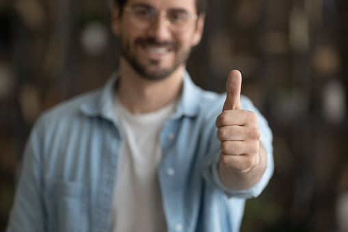 Crop close up blurred view of happy male client or customer show thumb up recommend good quality service or company. Smiling man feel satisfied pleased give recommendation. Review concept.