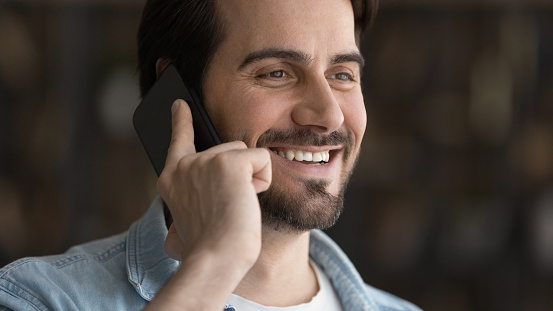 Wide banner panoramic view of smiling millennial Caucasian man have pleasant smartphone call with client or friend. Happy young male user talk speak on modern cellphone. Communication concept.