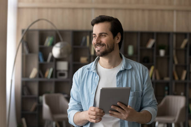 istock Smiling man use tablet dreaming at home 1294670729