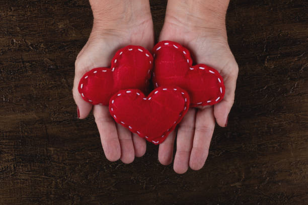 istock Female hand holding red hearts on rustic background. 1294671140
