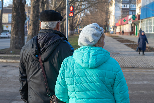 Dzhankoy, Republic of Crimea, January 2, 2021 - Elderly couple  walk down  street. Woman took her husband's under the hand. He tells her something  with smile.