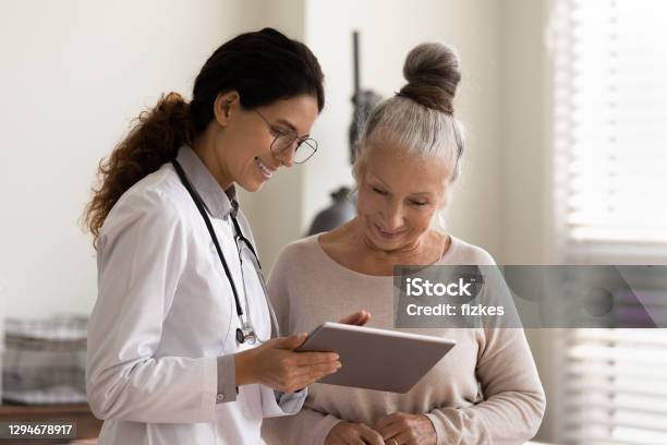 Happy Doctor And Senior Patient Use Tablet At Consultation - Fotografias de stock e mais imagens de Doutor