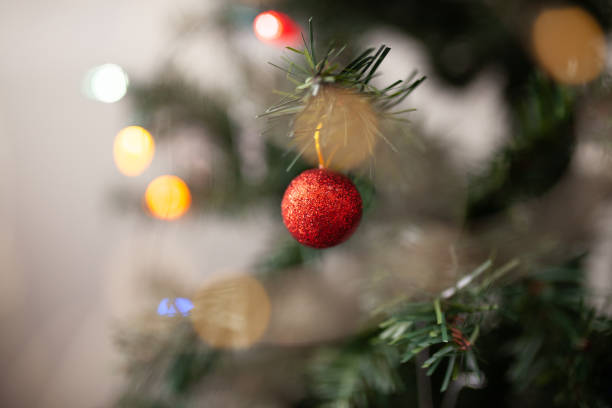 istock Red round Christmas tree ornament on green branch with copy space and string lights on the background. WInter holidays greeting card. Decorated Christmas tree close up 1294687011