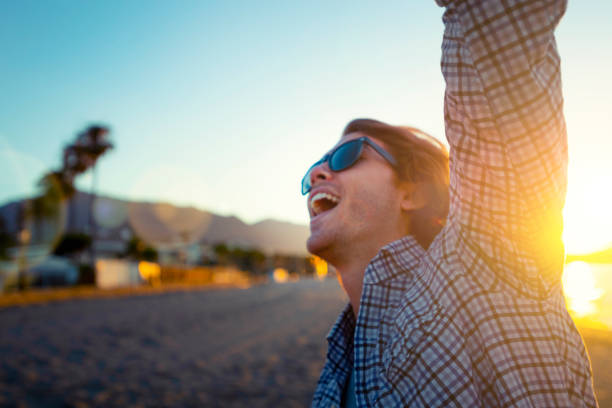 Man alone dancing and celebrating on the beach at sunrise/sunset. He is very happy, smiling and laughing.