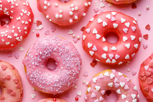 Sweet donuts with pink glaze decorating sprinkles on a pink background, top view.