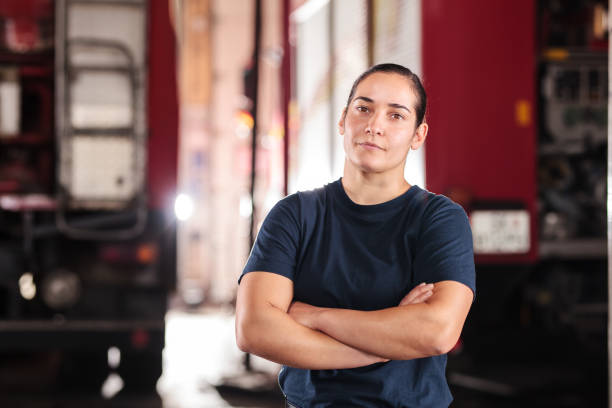 Professional fireman portrait. Female firefighter wearing uniform of shirt and trousers. Fire truck in the background. stock photo