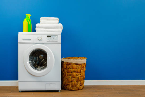 istock Washing machine with laundry on blue wall background 1294698811
