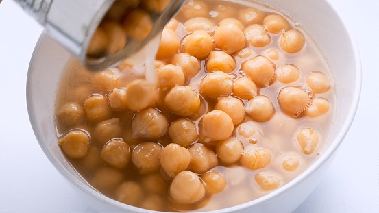 Pouring a can of organic garbanzo beans (chick peas) over a bowl