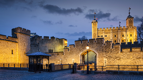 London, United Kingdom - March 23, 2018: Illuminated Tower of London Panorama. Public Street View to Bridge and Entrace Gate towards the Tower of London at Twilight. Illuminated iconic 11th-century White Tower in the background right. London, England, United Kingdom, Europe