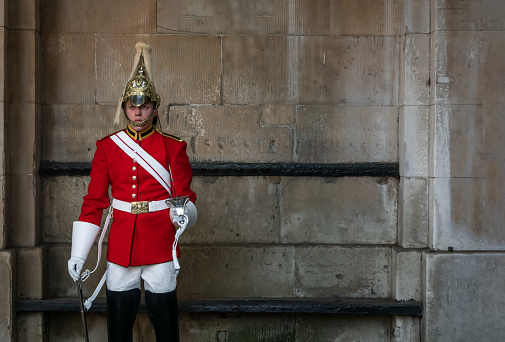 London, England - 19 Apr, 20 : A young Queen's Life Guard in full uniform with royal red coat and golden helmet stands at attention holding a sword at the Royal Palace. Copy space, Selective focus.