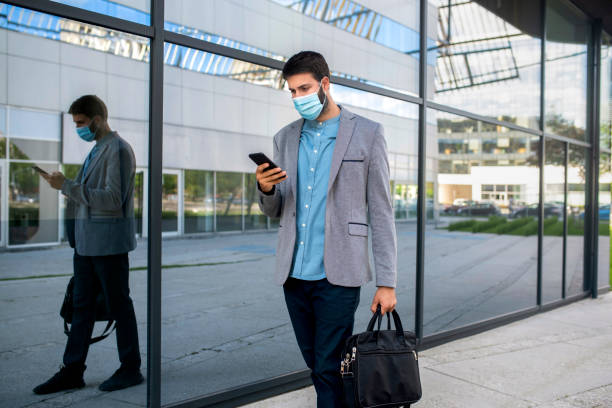 istock Businessman with a face mask goes to work during a lockdown and text the message on mobile phone stock photo 1294714838