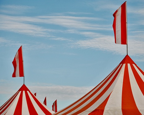 Orange and white striped circus tents photographed against a bright blue summer sky.