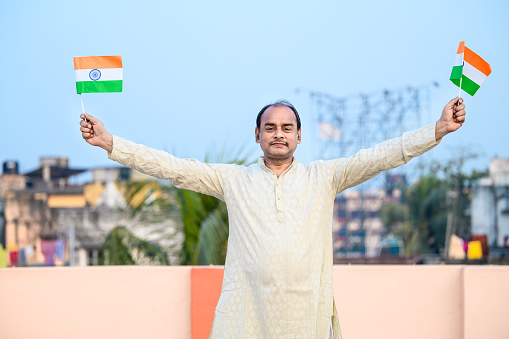 Outdoor image of Indian man waving Indian Flags in air and celebrating Independence or Republic day.