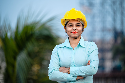 Close up portrait of beautiful female civil engineer wearing a protective helmet and looking at camera.