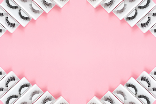 Different fake eyelashes on trendy pastel pink background. Beauty pattern. Makeup accessories. Cosmetics products for women. Top view, flat lay. Layout. Copy space. Place for text. Banner frame.