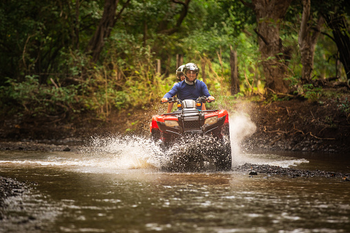 Dad and daughter crossing a small creek driving a 4x4 bike in Costa Rica