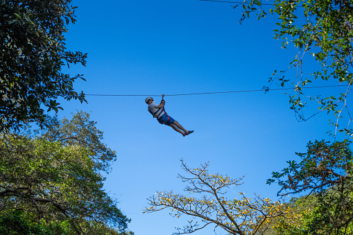 Hispanic man on a zip line in Costa Rica against blue sky